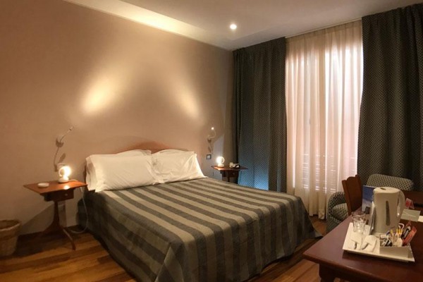 Pokój hotelowy z podwójnym łóżkiem i oświetlonymi stolikami nocnymi.