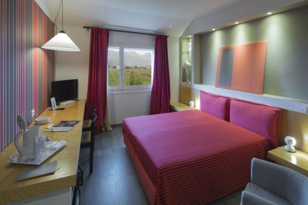 Nowoczesny pokój hotelowy z czerwonym łóżkiem, obok okna z widokiem na góry.