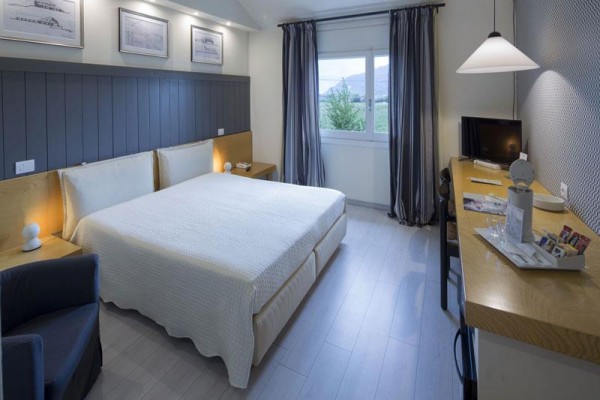 Nowocześnie urządzony pokój hotelowy z łóżkiem małżeńskim, biurkiem i telewizorem.