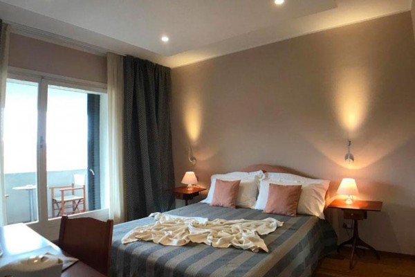 Pokój hotelowy z łóżkiem małżeńskim, stolikami nocnymi i drzwiami balkonowymi.