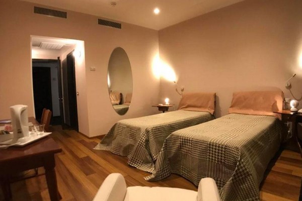Dwa pojedyncze łóżka w pokoju hotelowym z drewnianą podłogą i owalnym lustrem na ścianie.