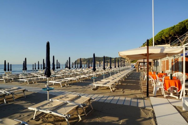 Plaża z rzędem pustych leżaków i zamkniętych parasoli w słoneczny dzień.