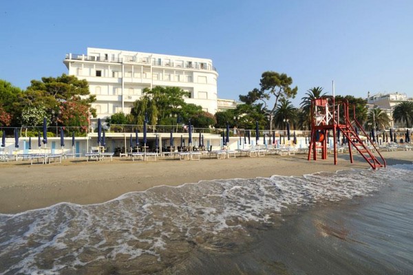 Plaża z leżakami, parasolami i wieżą ratowniczą, w tle hotel.