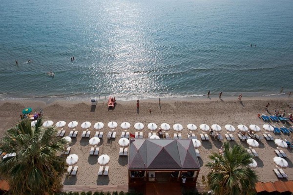 Plaża z leżakami i parasolami przy morzu, kilka osób w wodzie i na piasku.