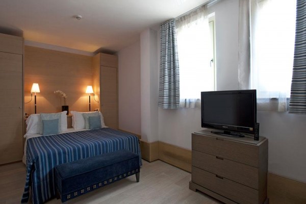 Pokój hotelowy z łóżkiem małżeńskim, telewizorem i dwoma lampami.
