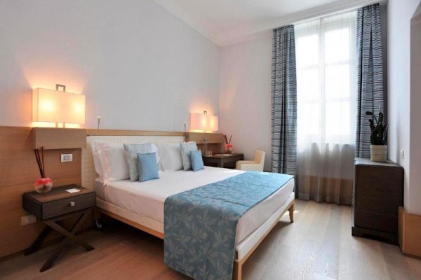 Nowoczesny pokój hotelowy z podwójnym łóżkiem, stolikami nocnymi i dużym oknem.