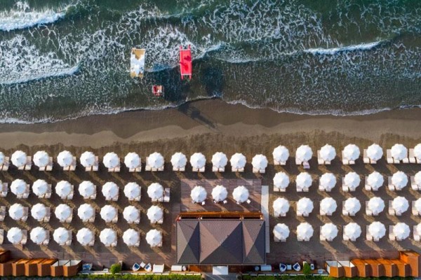 Plaża z rzędami białych parasoli i falami oceanu, widok z góry.
