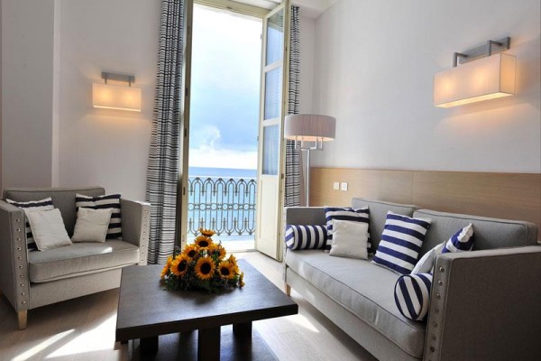 Jasny salon z kanapami i otwartymi drzwiami na balkon z widokiem na morze.