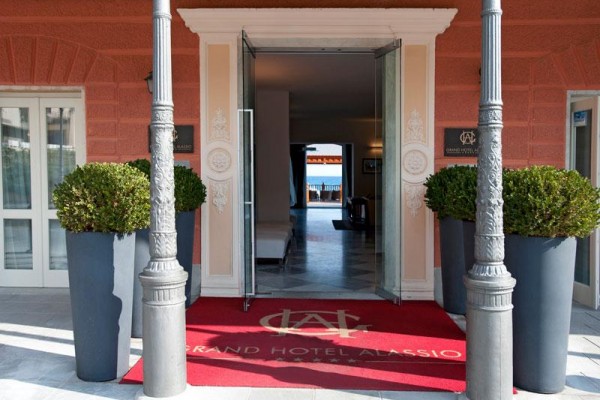 Wejście do Grand Hotelu Alassio z otwartymi szklanymi drzwiami i czerwonym dywanem.