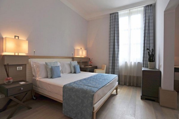 Nowoczesny pokój hotelowy z łóżkiem małżeńskim, stolikami nocnymi i dużym oknem.