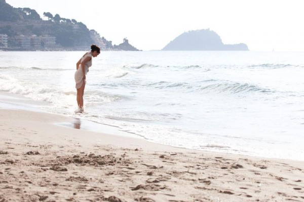 Osoba stoi na piaszczystej plaży przy morzu i patrzy na fale.