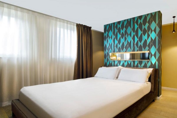 Nowoczesny pokój hotelowy z geometryczną tapetą za łóżkiem.