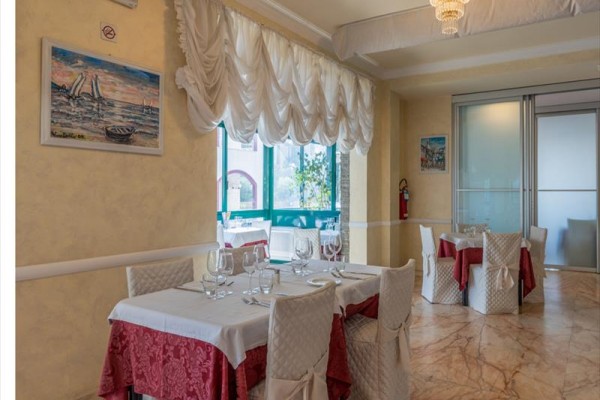 Restauracja z nakrytymi stołami, białymi obrusami i czerwonymi dodatkami.