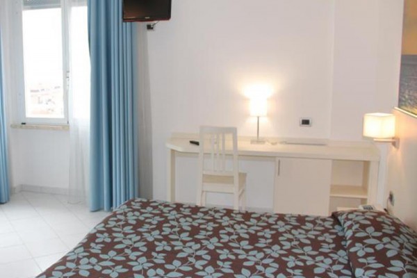 Pokój hotelowy z niebieskimi zasłonami, telewizorem, białym biurkiem i łóżkiem z brązową pościelą z niebieskim wzorem.