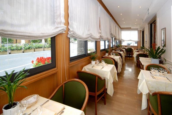 Restauracja z nakrytymi stołami i oknami z białymi zasłonami.