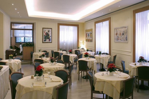 Restauracja z okrągłymi stołami, krzesłami i dekoracją kwiatową na stołach.