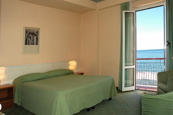 Pokój hotelowy z podwójnym łóżkiem i balkonem z widokiem na morze.