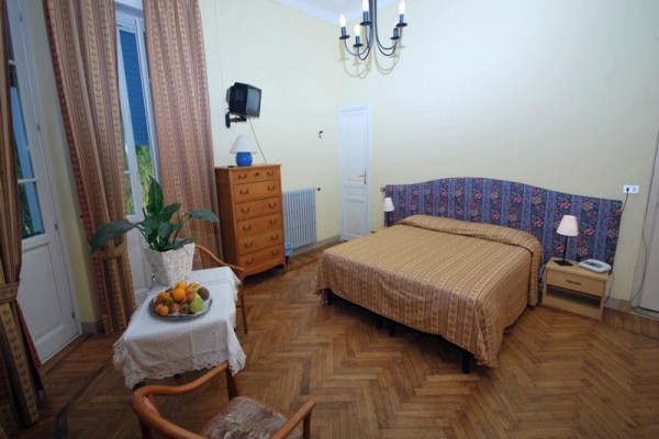 Sypialnia z żółtymi ścianami, łóżkiem, komodą, stołem z owocami i krzesłem.