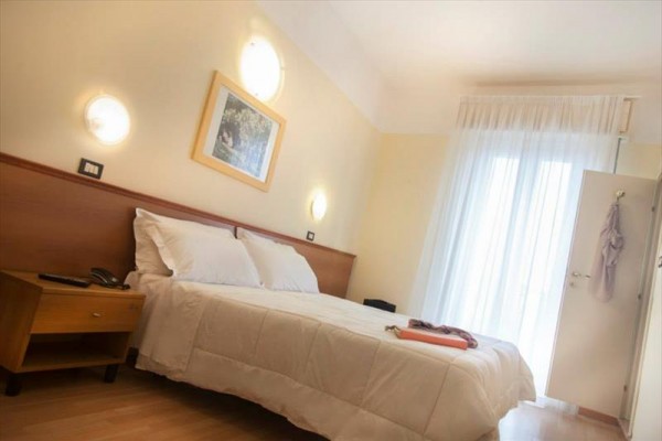 Jasny pokój hotelowy z podwójnym łóżkiem i stolikiem nocnym przy oknie z przezroczystymi zasłonami.