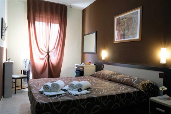 Pokój hotelowy z łóżkiem małżeńskim, brązowymi zasłonami i zapalonymi lampkami.