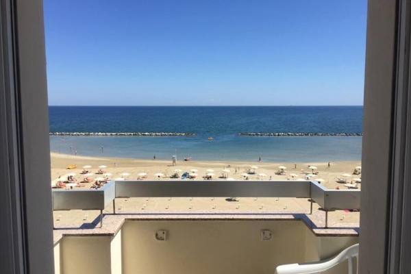 Widok na piaszczystą plażę z rozłożonymi parasolami, niebieskim morzem i czystym niebem z otwartego balkonu.