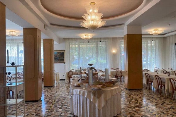 Elegancka restauracja z okrągłymi stołami, drewnianymi krzesłami i sufitowymi lampami.