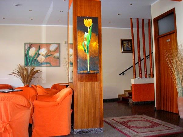 Lobby hotelowa z pomarańczowymi fotelami i obrazami kwiatów na ścianach.