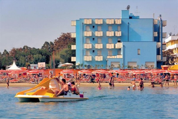 Ludzie na rowerze wodnym na morzu przed plażą z niebieskim budynkiem w tle.