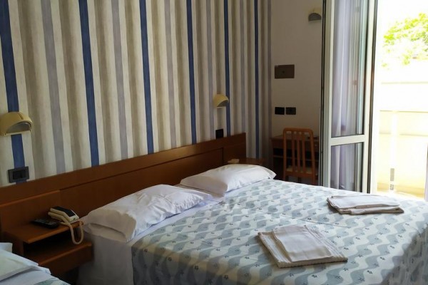 Pokój z dwoma łóżkami, paskowanymi tapetami i otwartymi drzwiami na balkon.