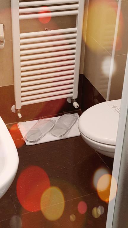Łazienka z toaletą, grzejnikiem i kapciami na macie.