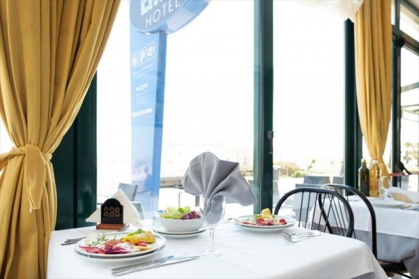 Stoliki w restauracji z nakrytym obrusem i elegancko złożoną serwetką, obok okna z widokiem na zewnątrz.