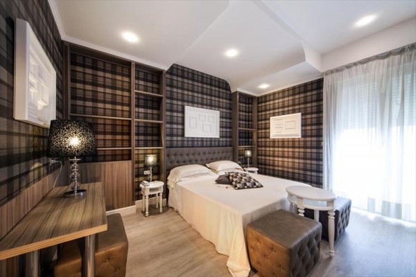 Nowoczesny pokój hotelowy z łóżkiem małżeńskim i kratkowaną tapetą na ścianach.