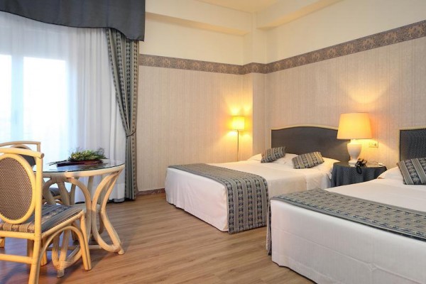 Pokój hotelowy z dwoma pojedynczymi łóżkami, małym okrągłym stolikiem i dwoma krzesłami.