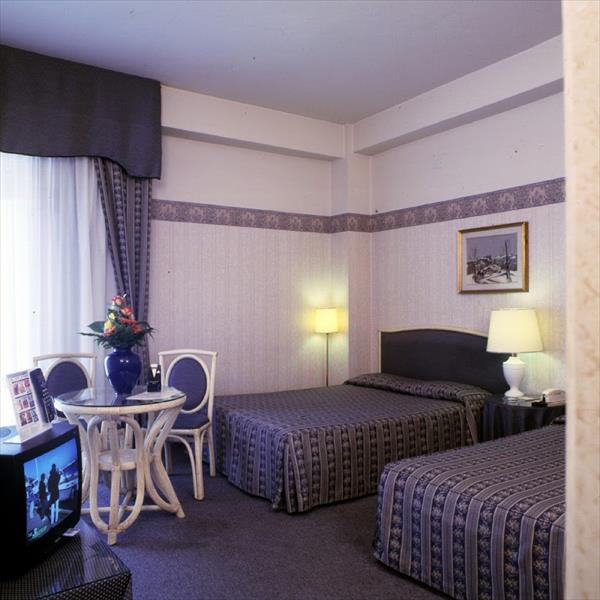 Pokój hotelowy z dwoma łóżkami, stolikiem i telewizorem.