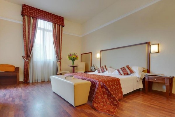 Elegancki pokój hotelowy z łóżkiem małżeńskim, oknem z długimi zasłonami i bukietem na stole.