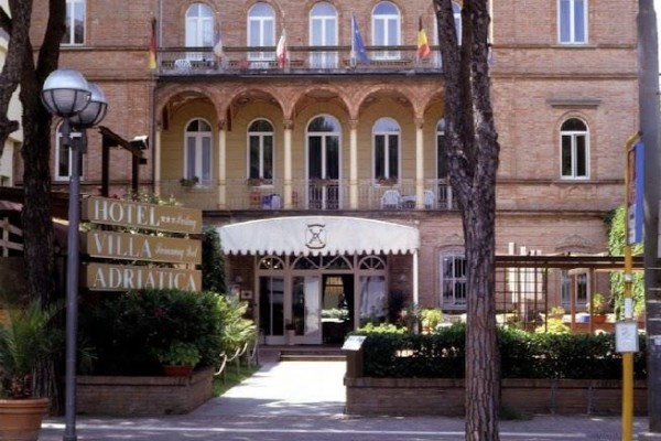 Hotel Villa Adriatica z ceglaną fasadą i balkonami, otoczony drzewami.