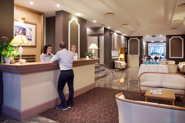 Recepcja w holu hotelowym z mężczyzną rozmawiającym z recepcjonistką.