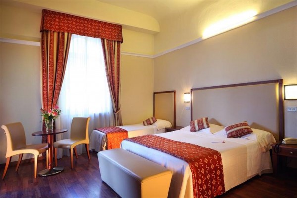 Pokój hotelowy z łóżkiem małżeńskim, pojedynczym łóżkiem i kącikiem wypoczynkowym z dwoma krzesłami.