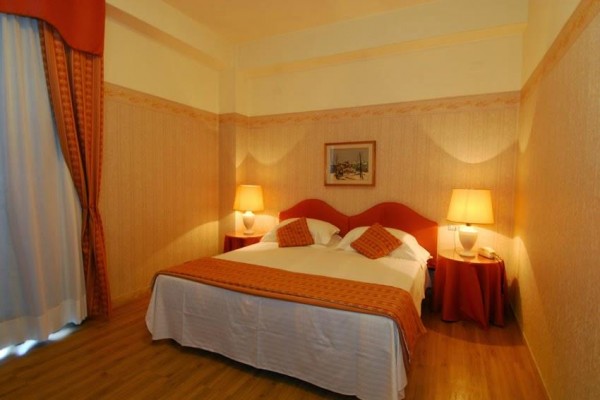 Pokój hotelowy z podwójnym łóżkiem, dwiema lampami i pomarańczowymi dekoracjami.