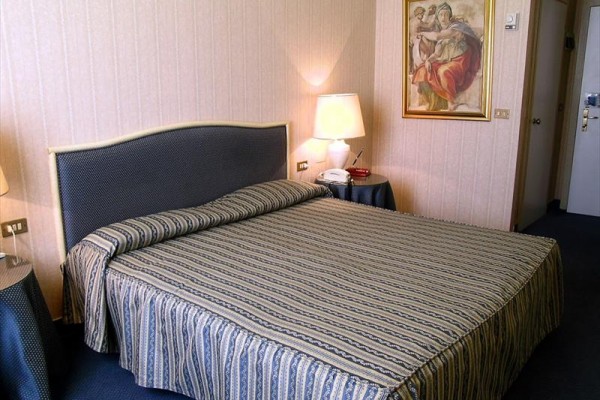 Pokój hotelowy z łóżkiem małżeńskim, lampą i obrazem na ścianie.