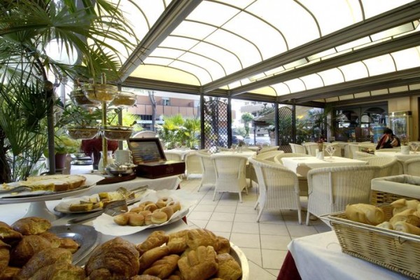 Zadaszona restauracja na świeżym powietrzu z białymi meblami i serwowanym pieczywem.