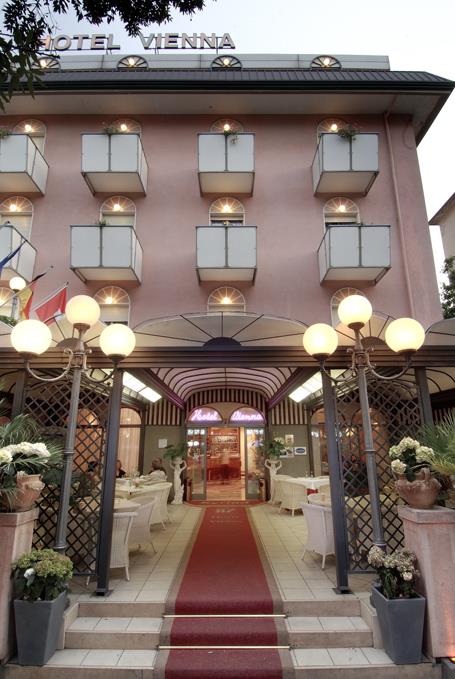 Wejście do hotelu z czerwonym dywanem i zewnętrznymi miejscami do siedzenia.