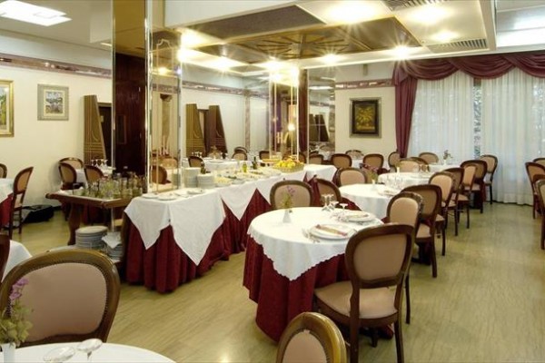 Elegancka restauracja z okrągłymi stołami przykrytymi białymi obrusami i brązowymi krzesłami.