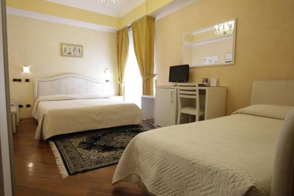 Pokój hotelowy z dwoma łóżkami, biurkiem i zasłonami w jasnych żółtych odcieniach.