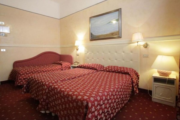 Trzy łóżka w hotelowym pokoju z czerwonymi narzutami.