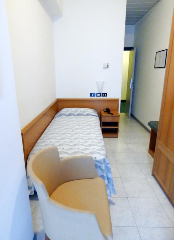 Pokój jednoosobowy z łóżkiem, krzesłem i stolikiem nocnym.
