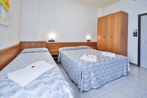 Pokój hotelowy z dwoma łóżkami, stolikami nocnymi i szafą.