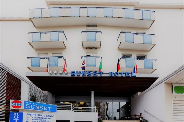 Budynek hotelu Sunset z szklanymi balkonami i wejściem, na którym wiszą liczne flagi.