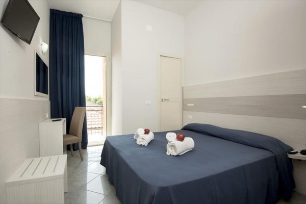 Mały pokój hotelowy z podwójnym łóżkiem i niebieską narzutą.