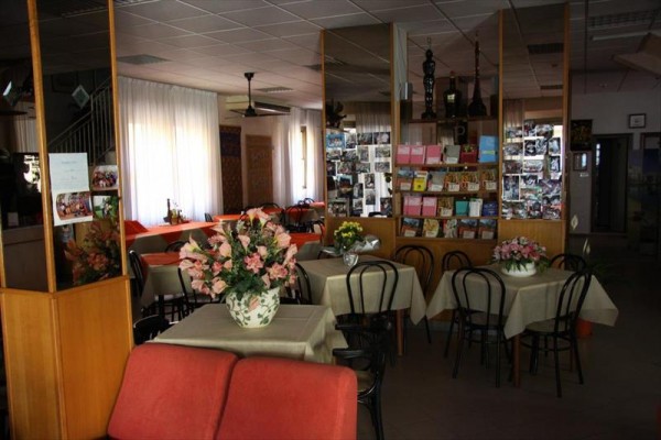 Restauracja z kwiatami na stołach i stojakiem z pocztówkami.